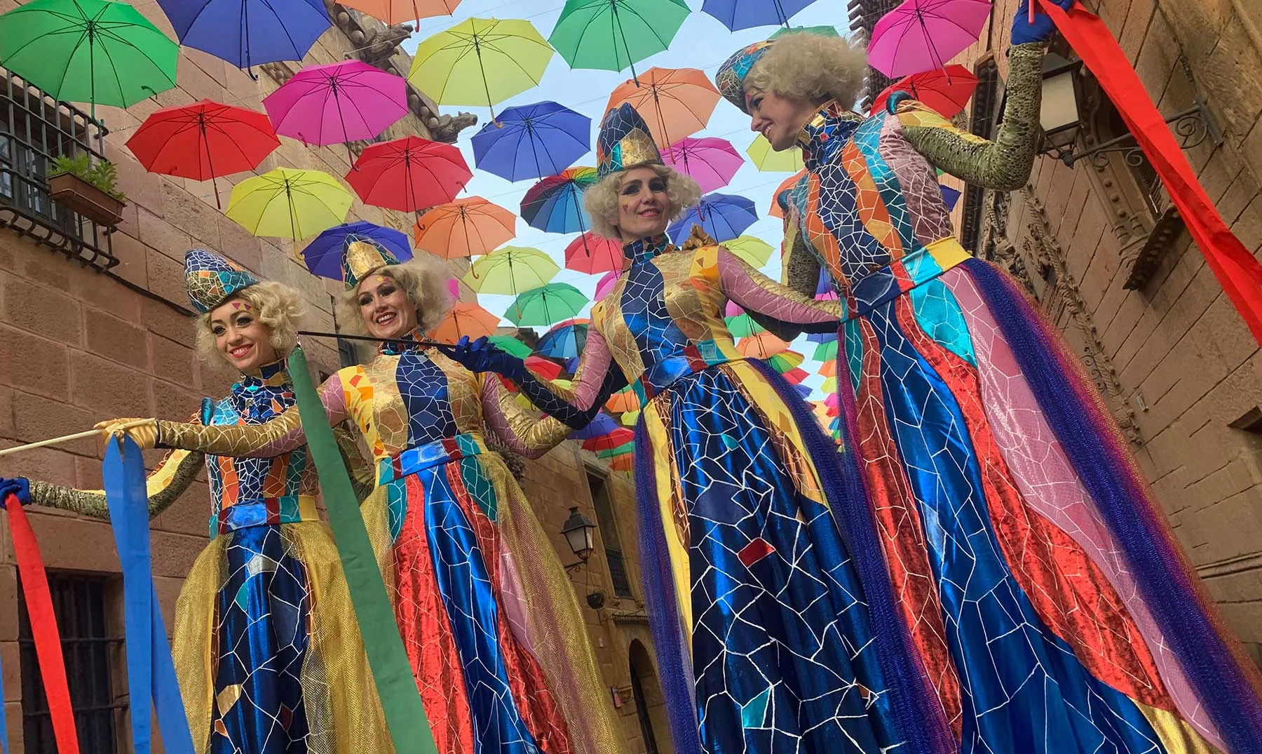 Échassiers en costumes colorés sous une voûte d’ombrelles multicolores