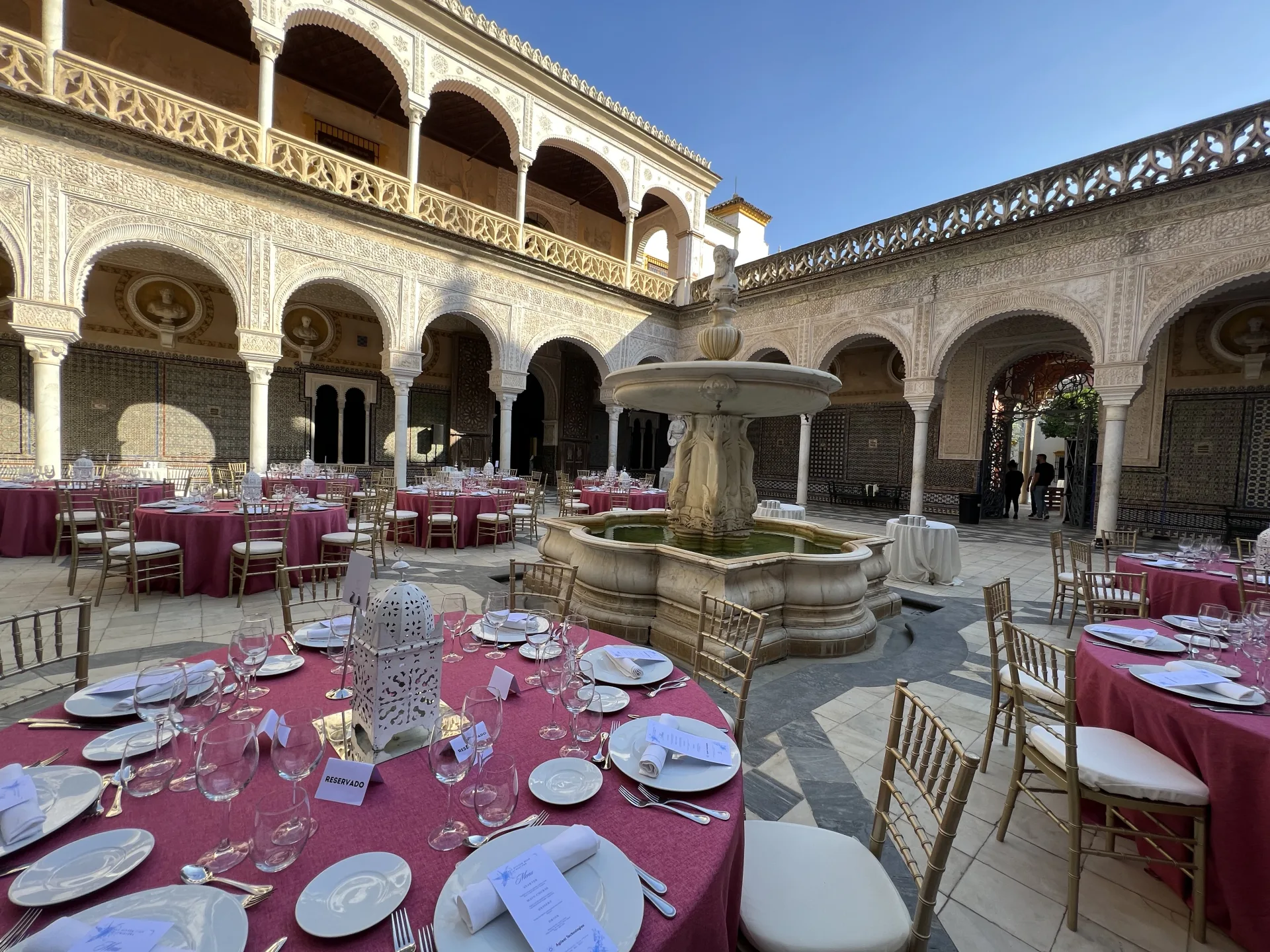 Banquet dressé autour de la fontaine d’un patio à arcades sévillan, nappes fuchsia