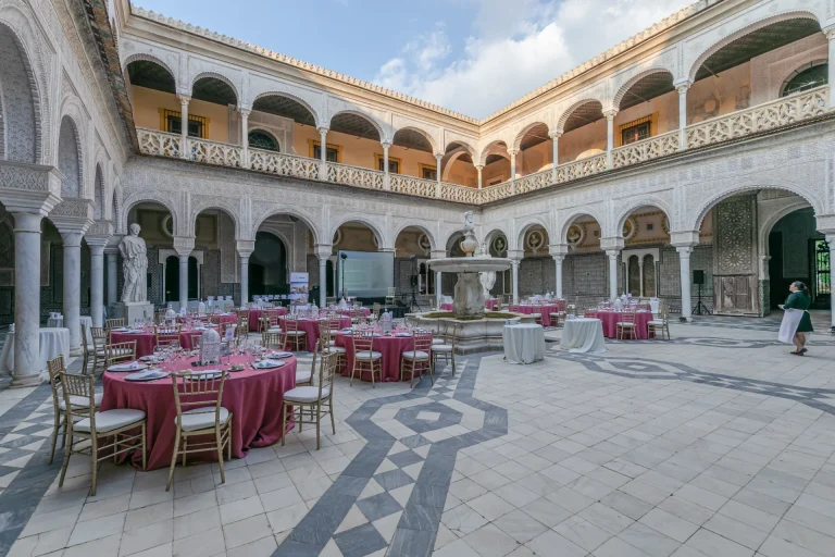 Tables rondes fuchsia dressées dans le patio à arcades d’un palais sévillan