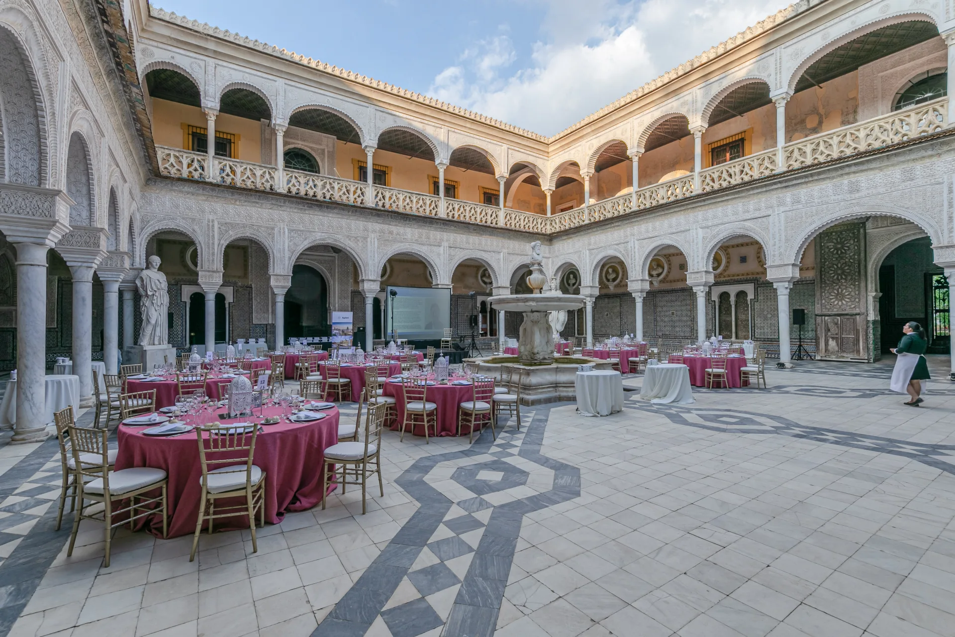 Tables rondes fuchsia dressées dans le patio à arcades d’un palais sévillan
