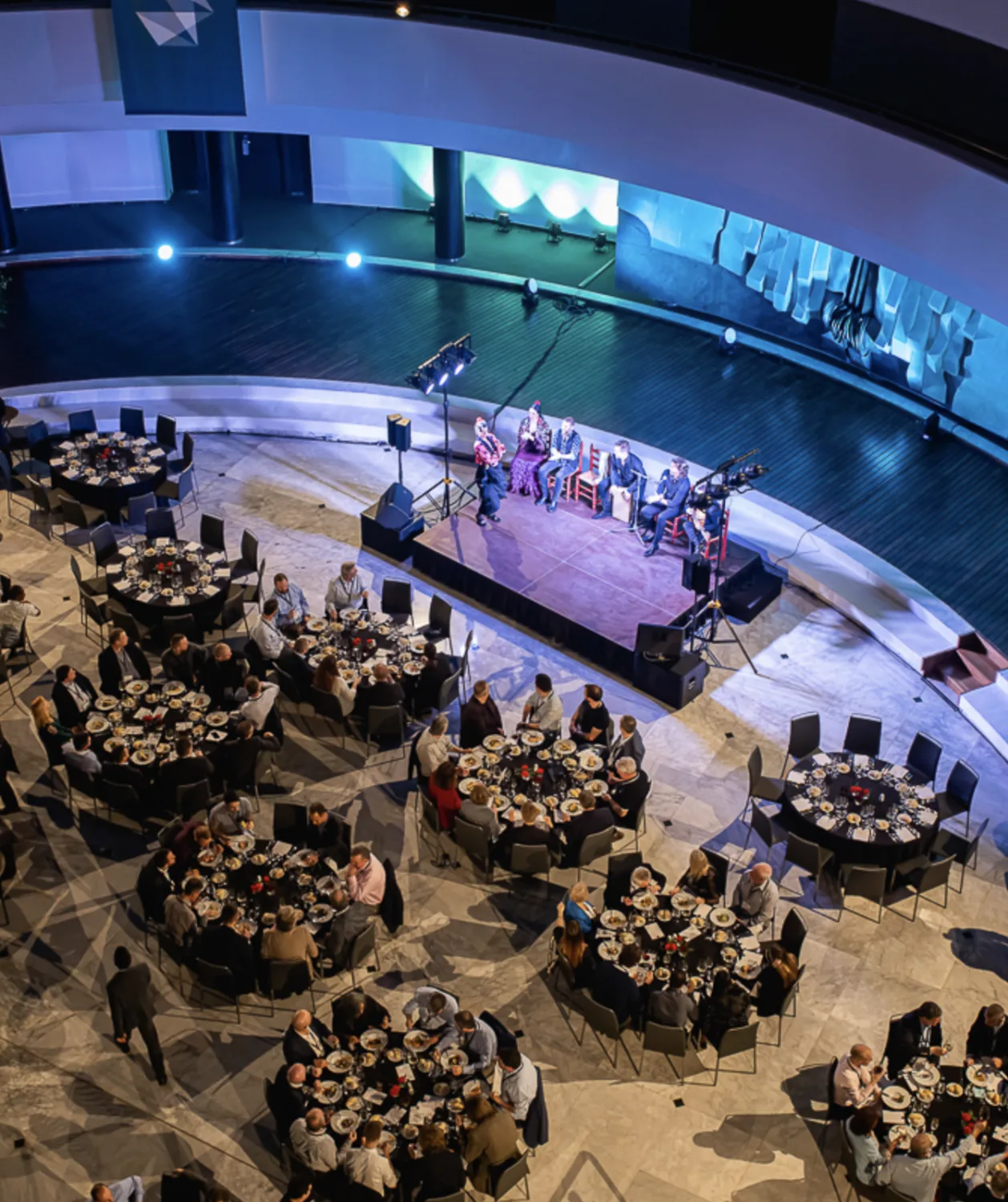Vue plongeante sur une salle de spectacle et ses tables rondes pendant un dîner-show