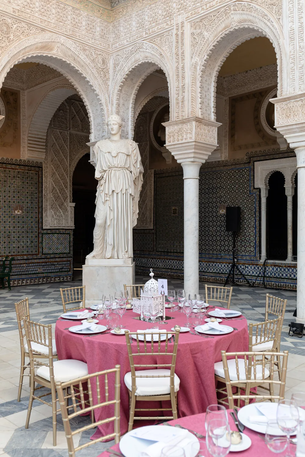 Tables fuchsia dressées autour d’une statue dans un patio à colonnes
