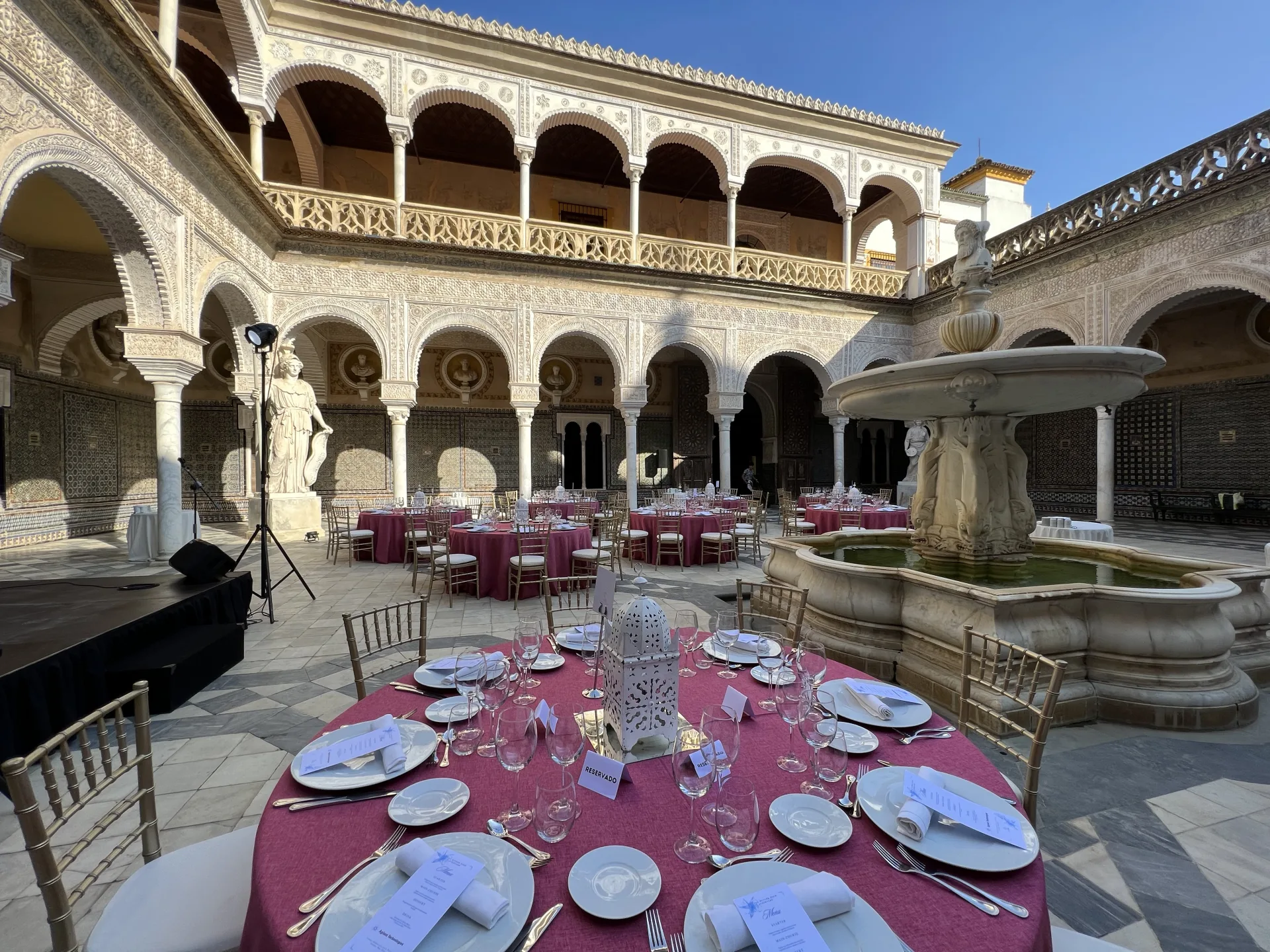 Tables rondes fuchsia dressées dans le patio à arcades d’un palais sévillan
