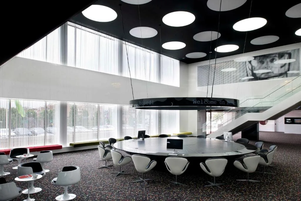 Salle de réunion design en noir et blanc, grande table ovale sous un plafond ajouré