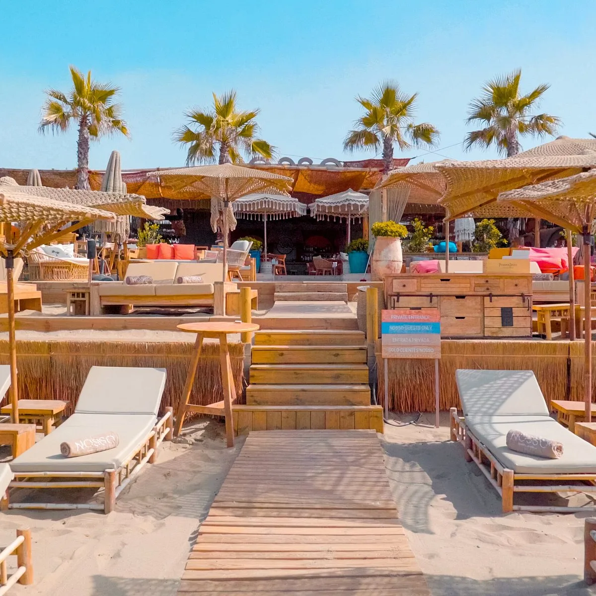 Beach club coloré, transats et bar en bois face à la plage