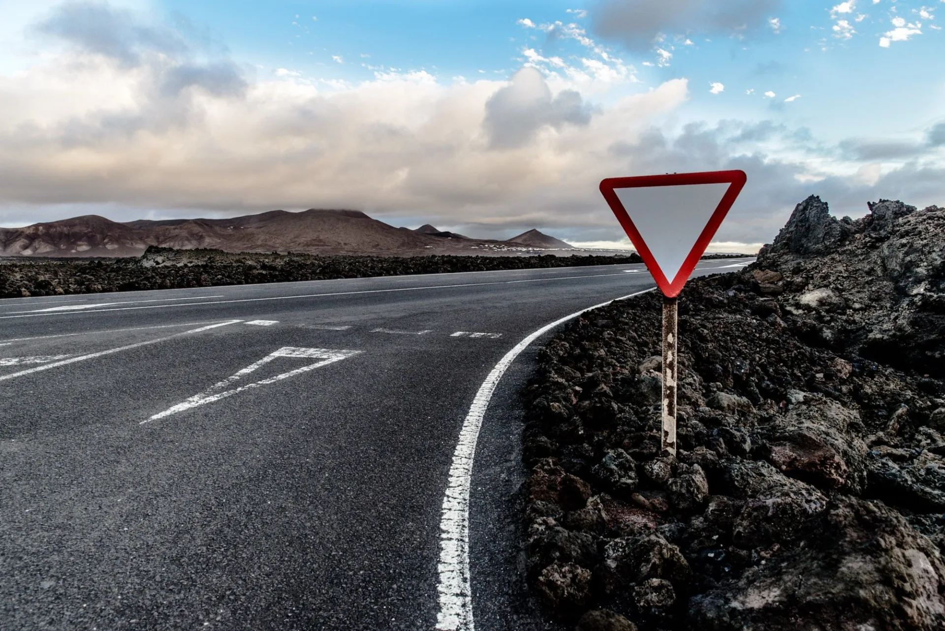 Route traversant un champ de lave sous un ciel nuageux, à Lanzarote